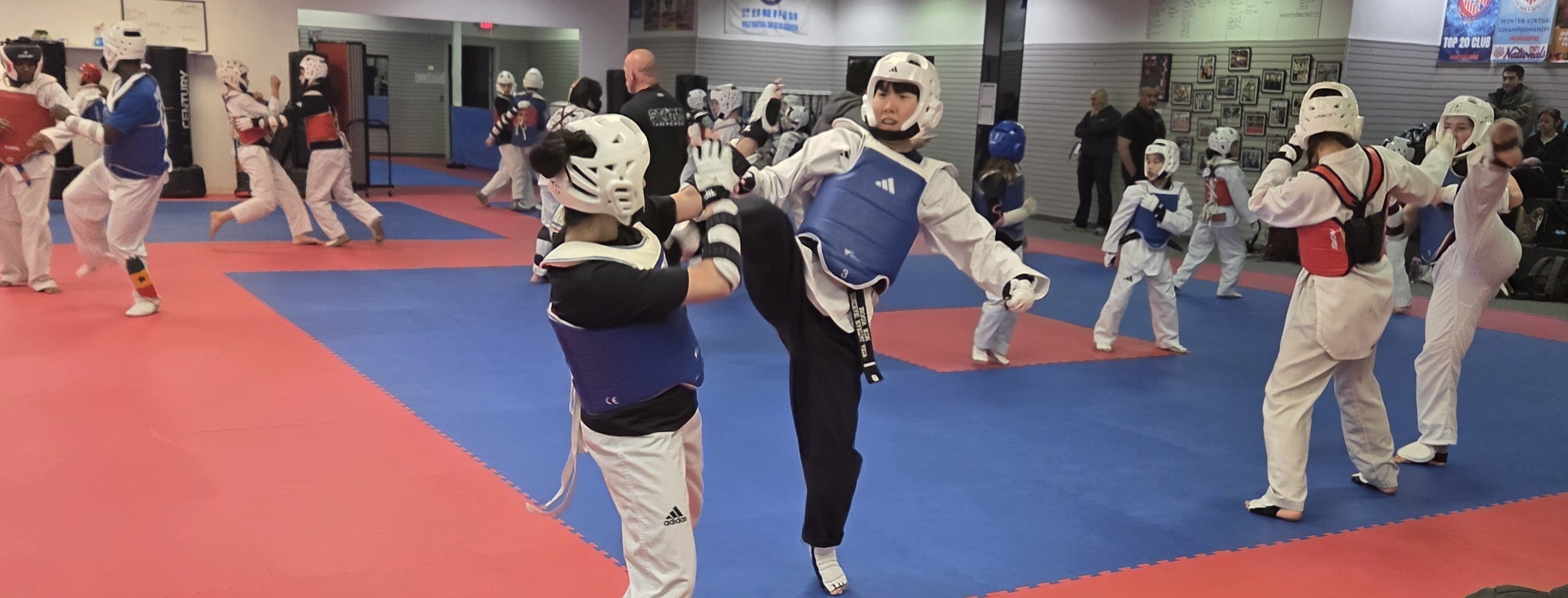 Karate class in progress with students wearing protective gear on a red and blue mat.