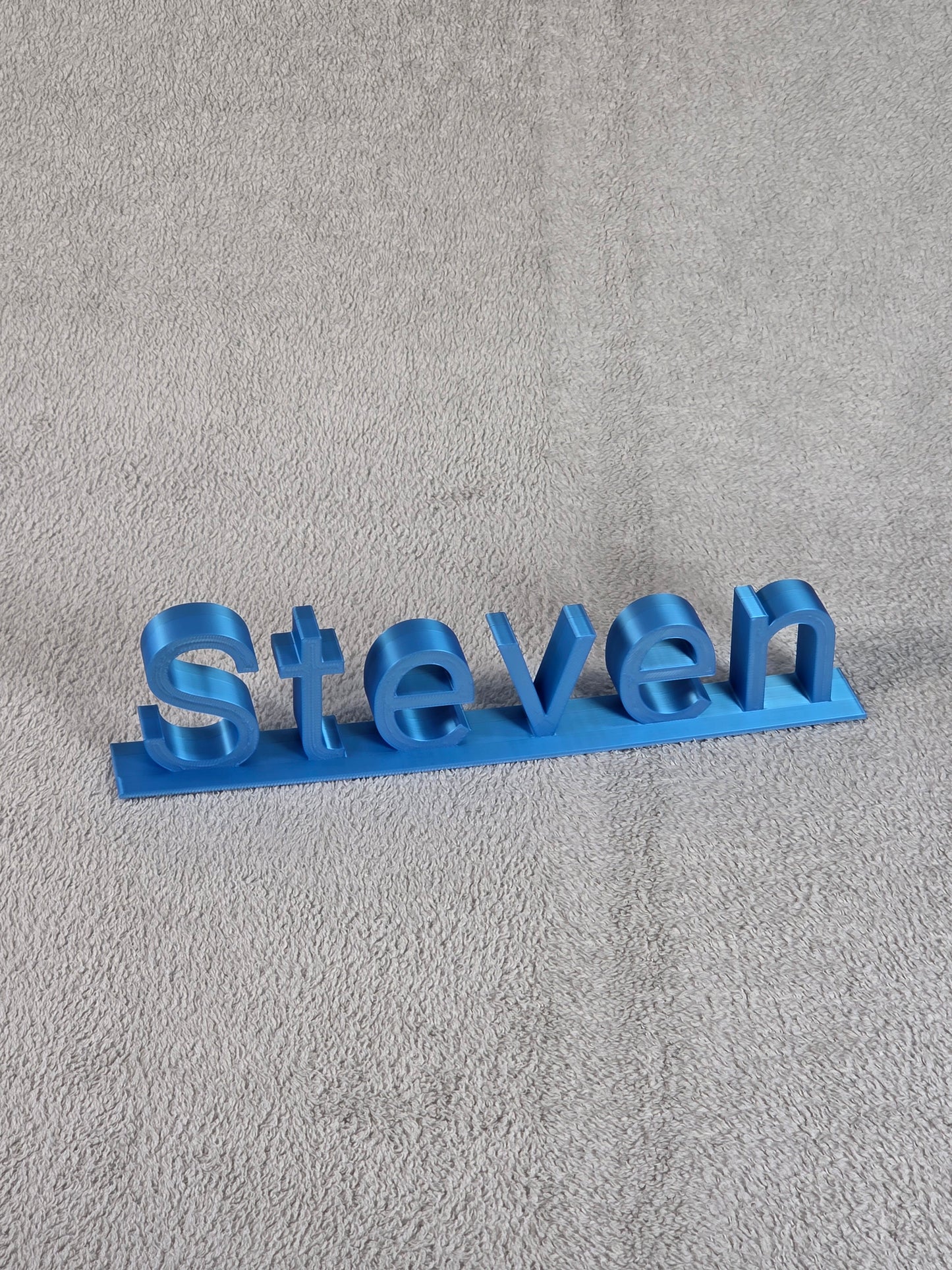 Blue 3D-printed name 'Steven' on a gray textured background