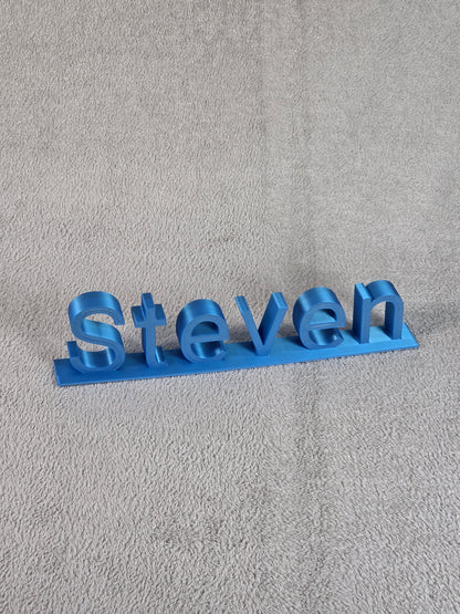 Blue 3D-printed name 'Steven' on a gray textured background