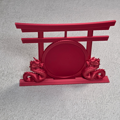 Red decorative topper with dual dragons facing each other next to a round patch area in front of a torii gate on a light gray background